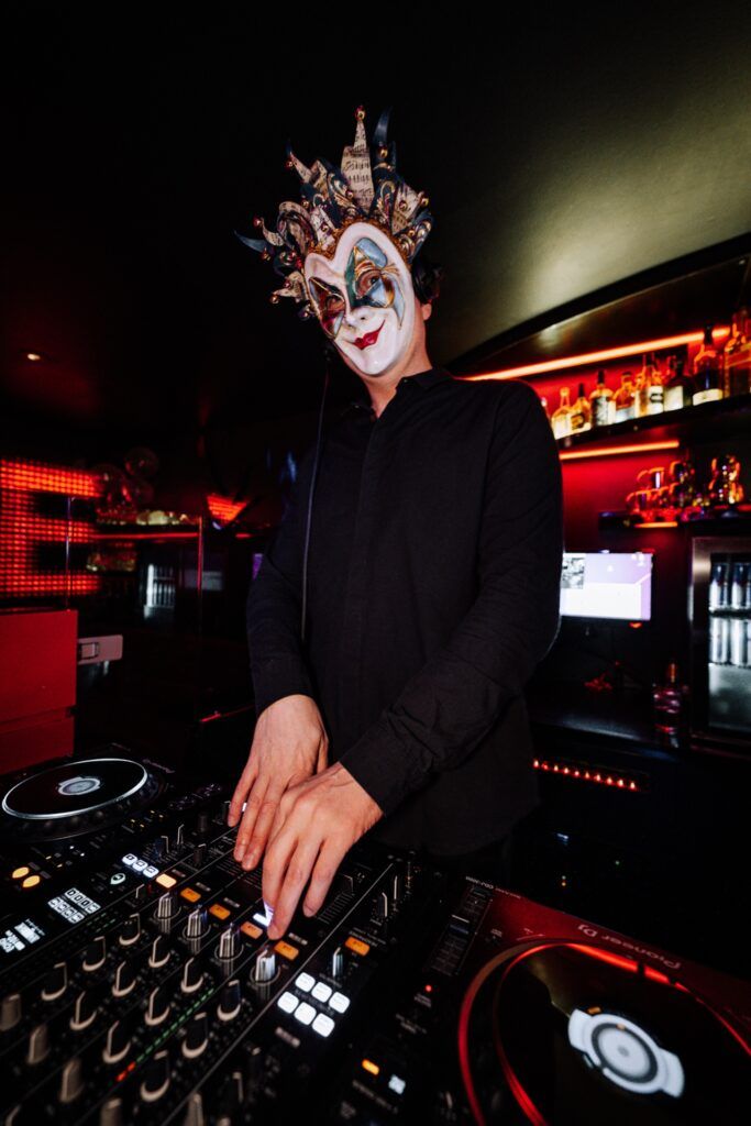 Ein maskierter DJ bedient ein Mischpult in einem Club.